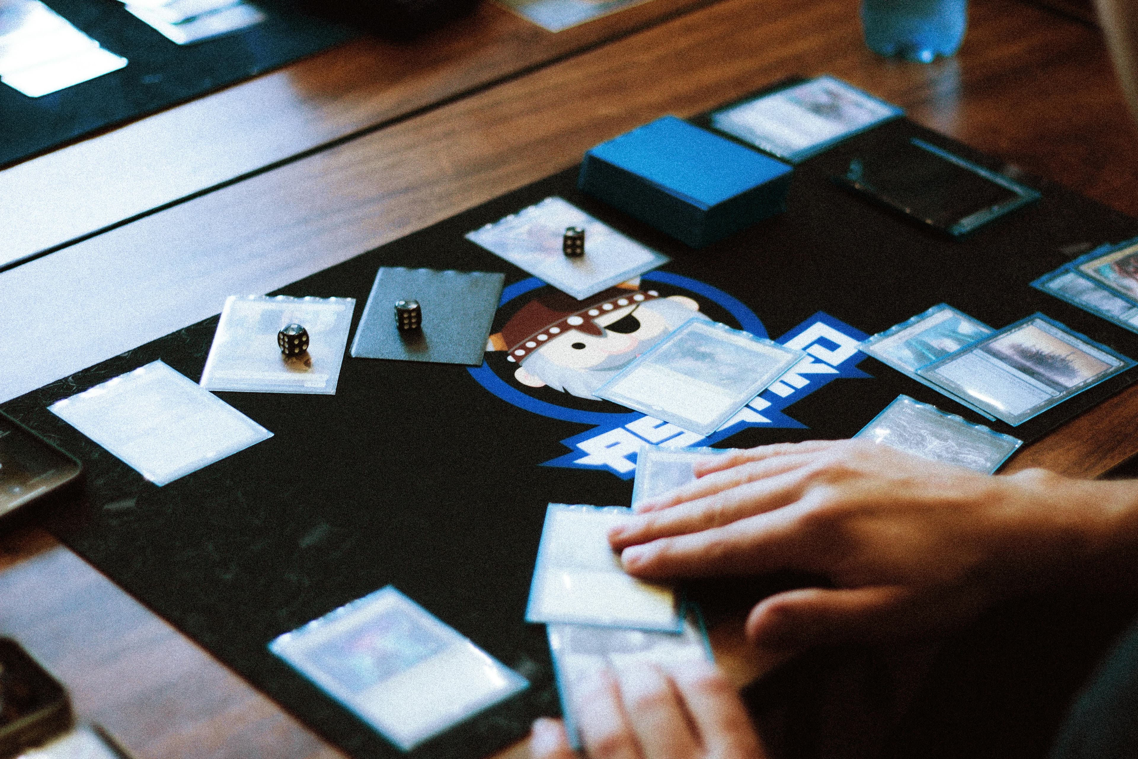 Tabletop card game with sleeved cards and dice on a play mat.